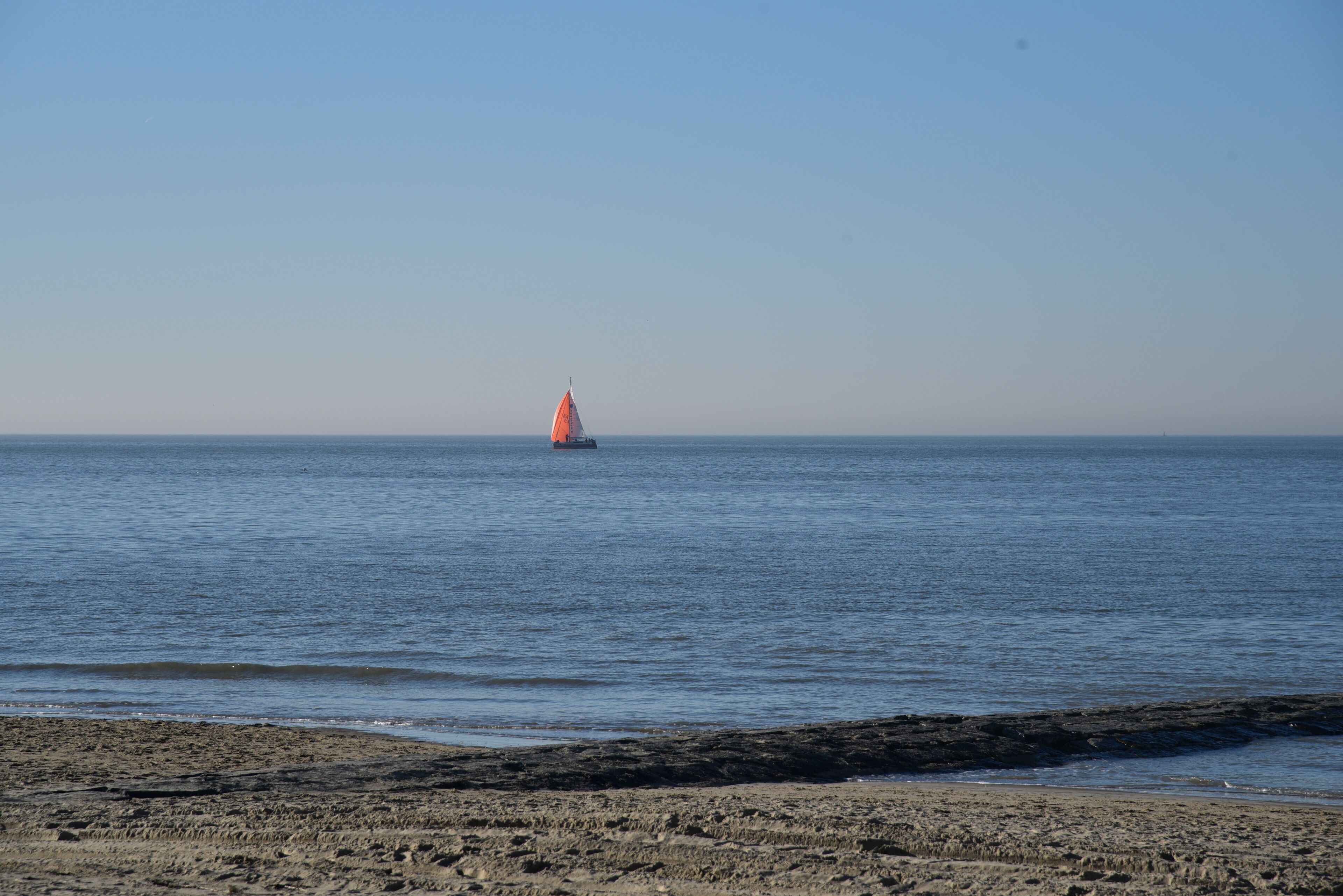 A sandy beach with a sailboat in the distance.