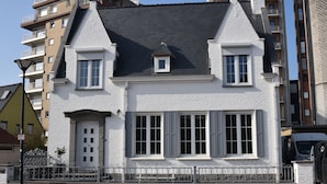 Un edificio blanco con techo a dos aguas, dos ventanas con contraventanas y un pequeño dormer.