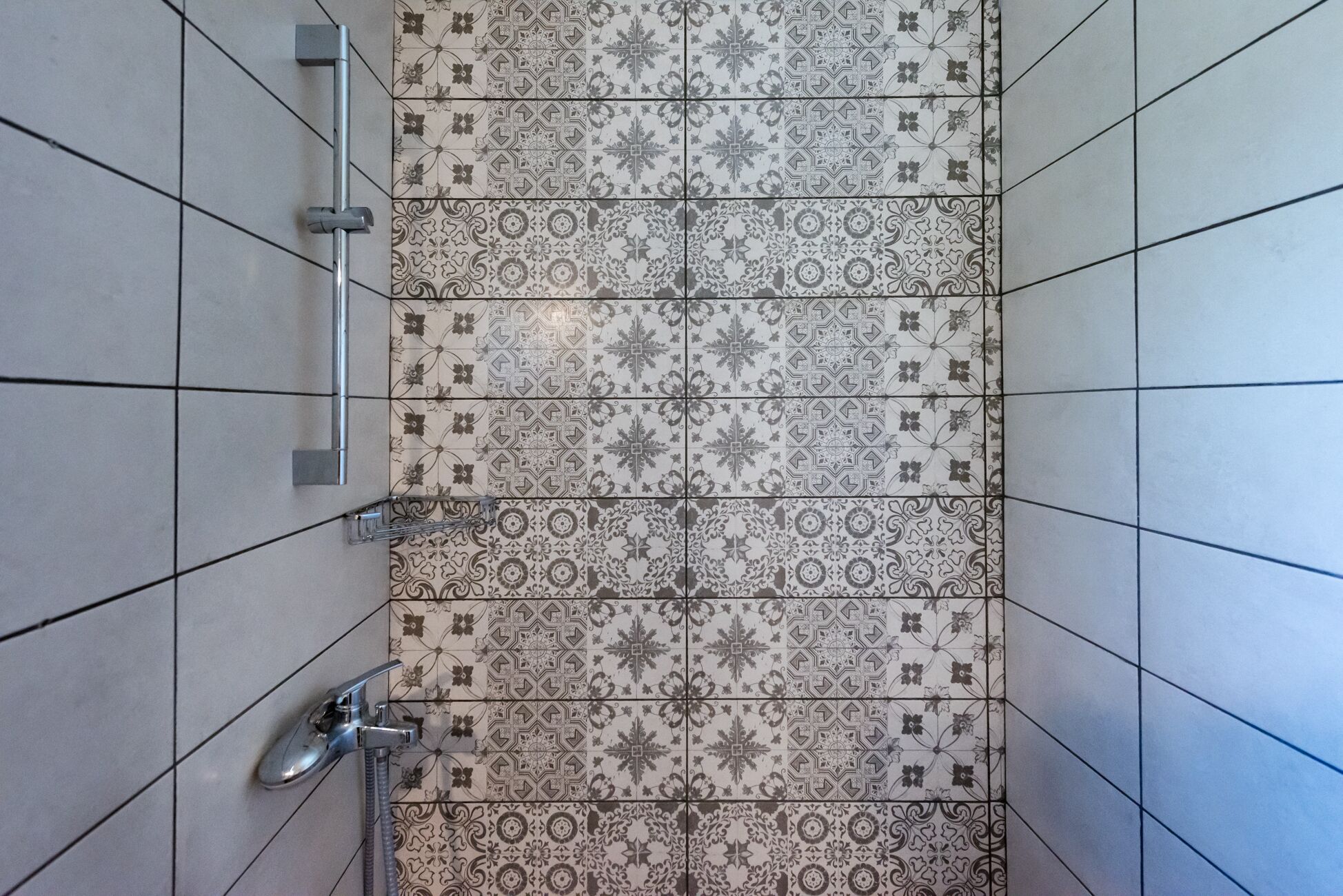 A bathroom with a tiled floor featuring a variety of patterns and a shower area with a faucet and hose.