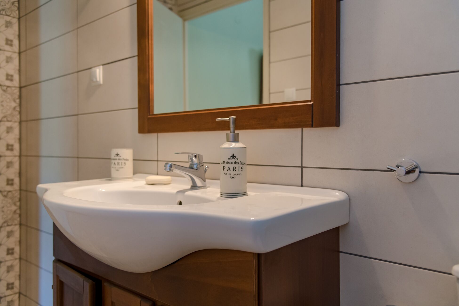 A bathroom with a white sink, a mirror, and a bottle of perfume.