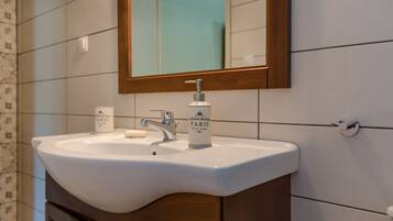 A bathroom with a white sink, a mirror, and a bottle of perfume.