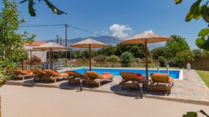 A poolside area with lounge chairs and umbrellas, a clear sky, and mountains in the background. - It is our pleasure to welcome you to Kefalonia Island and invite you to enjoy yo (kefalonia)