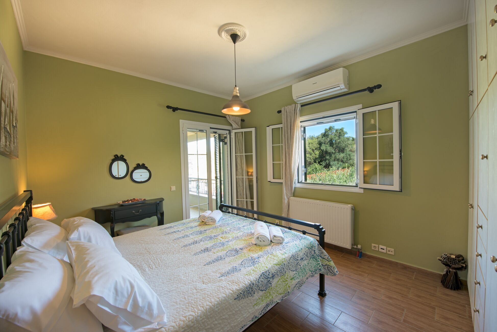 Ein Schlafzimmer mit Bett, Nachttisch, Kommode, einem Fenster mit Vorhängen, einer Klimaanlage und einem Heizkörper.