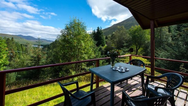 Une terrasse en bois avec une table et des chaises, offrant une vue sur un paysage montagneux avec un lac.