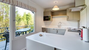 Une cuisine moderne dotée d’une grande fenêtre, un coin repas avec une table et des chaises, et une vue sur les arbres à l’extérieur.