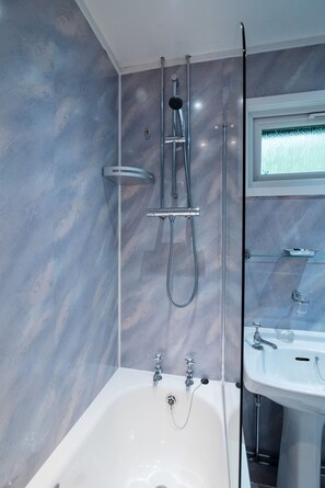 Un bany modern amb dutxa de vidre, banyera blanca i prestatge de vidre sobre el lavabo.