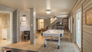 Una habitación amplia con mesa de fútbol, mesa de ping pong y un altillo con televisor.