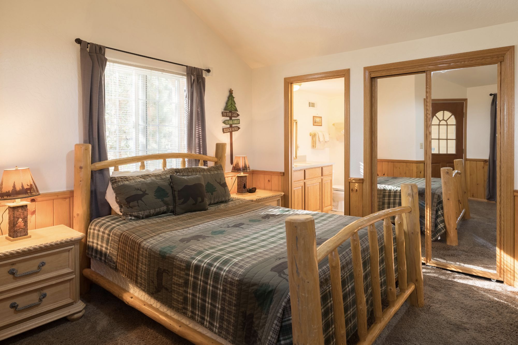 A bedroom with a wooden bed, a nightstand, a lamp, a mirror, and a window with curtains.