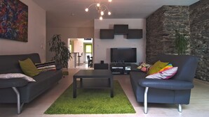 A modern living room with a sofa, coffee table, and TV. There is a stone wall and a painting on the wall. - Modern 5-star luxury in a historic setting (Boppard)