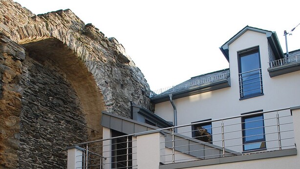 A modern two-story house with a stone archway entrance, a balcony, and a small attached garage. - Modern 5-star luxury in a historic setting (Boppard)