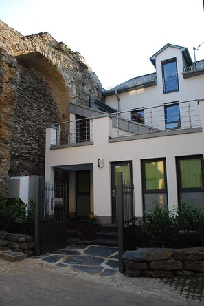 Une maison moderne à deux étages, dotée d’une entrée en arc de pierre, d’un balcon et d’un petit garage attenant.