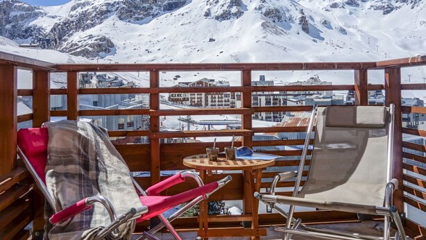 En träveranda med ett bord och stolar, med utsikt över ett snöklätt berglandskap.