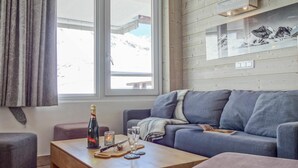 Ett modernt vardagsrum med en grå soffa, ett träbord och ett fönster med utsikt över snöklädda berg.