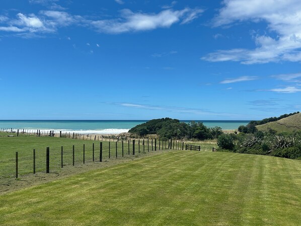 Un campo cubierto de hierba con una cerca, una playa y un cielo azul despejado.