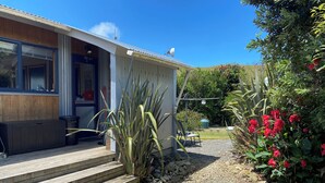 A house with a wooden deck, a gravel pathway, and a garden with red flowers. - 'Time Out'  Beach Front getaway with amazing sea views (Whangaehu Beach)