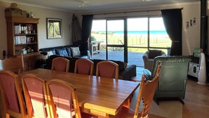 A dining area with a wooden table and chairs, a sofa, and a bookshelf. - 'Time Out'  Beach Front getaway with amazing sea views (Whangaehu Beach)