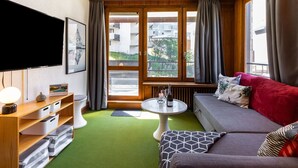 Una sala moderna con alfombra verde, un sofá, una mesa de centro, un televisor y una ventana con cortinas.