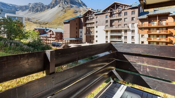 Terraza de madera con vistas a una zona montañosa y edificios modernos.