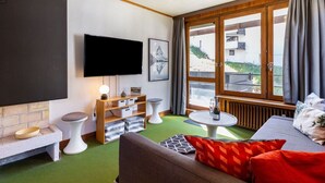 Una sala de estar acogedora con una televisión de pantalla plana, chimenea, sofá, mesa de centro y ventana con cortinas.