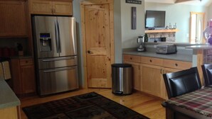 Una cucina con mobili in legno, un frigorifero in acciaio inossidabile, un cestino e un'area pranzo con tavolo e sedie.