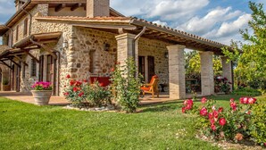 A stone house with a covered patio, a chimney, and a garden with flowers and a lawn. - Cosy apartment for 6 people with WIFI, pool, TV, patio, pets allowed and panoramic view (Allerona)
