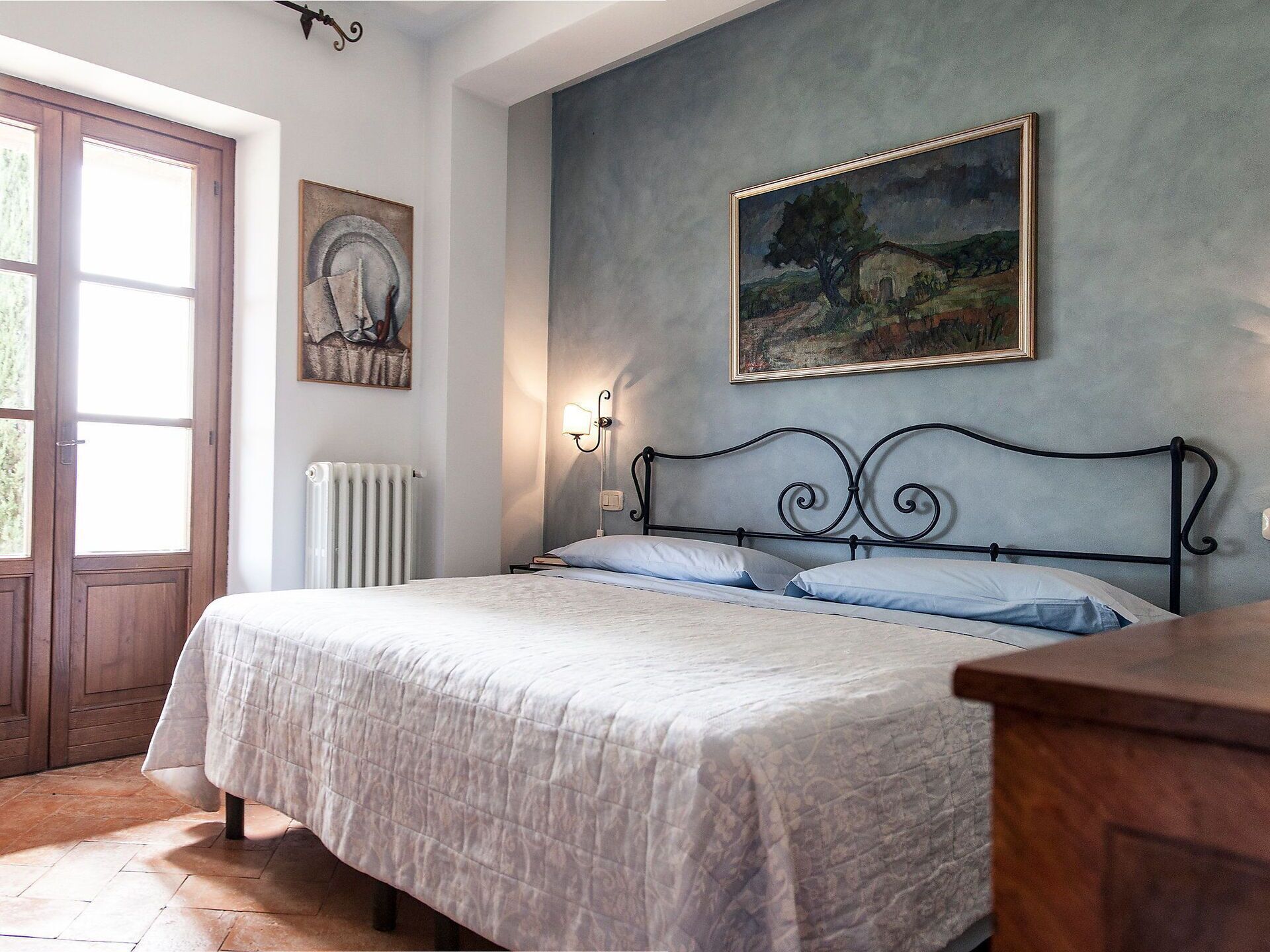 Un dormitorio con una cama, un radiador, una ventana y un cuadro en la pared.