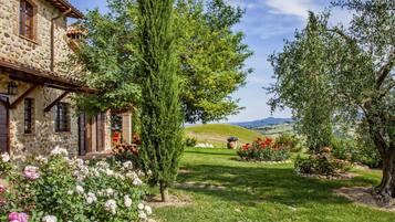 Una casa di pietra con un giardino, un albero alto e vista su dolci colline.