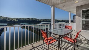 Ein Balkon mit Tisch und Stühlen mit Blick auf ruhiges Wasser und bewaldetes Gebiet.