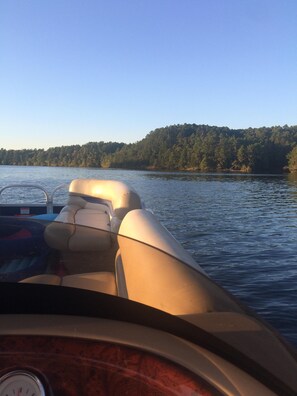 Ein Boot mit Holldeck und Steuer, umgeben von ruhigem Wasser und einer bewaldeten Uferlinie.