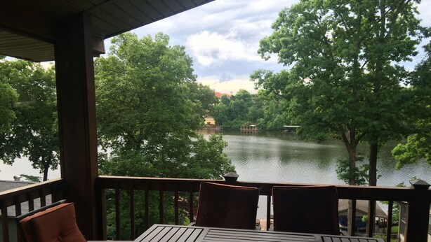 A covered outdoor seating area with a table and chairs, overlooking a lake with trees and a gazebo. - Stan's Lake Hamilton II, MainChannel, Kayaks, Fire Pit, Swim/Boat Dock, Pontoon (Hot Springs)