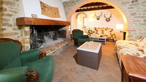 Un intérieur rustique avec des murs en pierre, une cheminée, des fauteuils à revêtement vert, un canapé à motifs et des décorations en forme de bois de cerf.