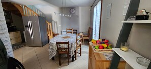 A compact kitchen with a refrigerator, dining table, chairs, and a fruit basket. - House of 100 m2 on a 2500 m2 fenced (Cierp-Gaud)