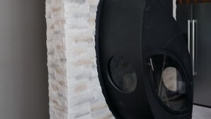 A corner of a room with a white brick wall, a black hanging chair, and a small table with a bowl. - House of 100 m2 on a 2500 m2 fenced (Cierp-Gaud)