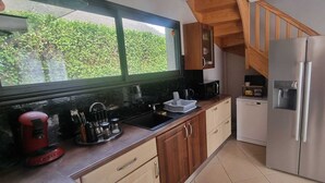 A kitchen with a stainless steel refrigerator, a microwave, a sink, and a coffee maker. There is a wooden staircase leading to an upper level. - House of 100 m2 on a 2500 m2 fenced (Cierp-Gaud)