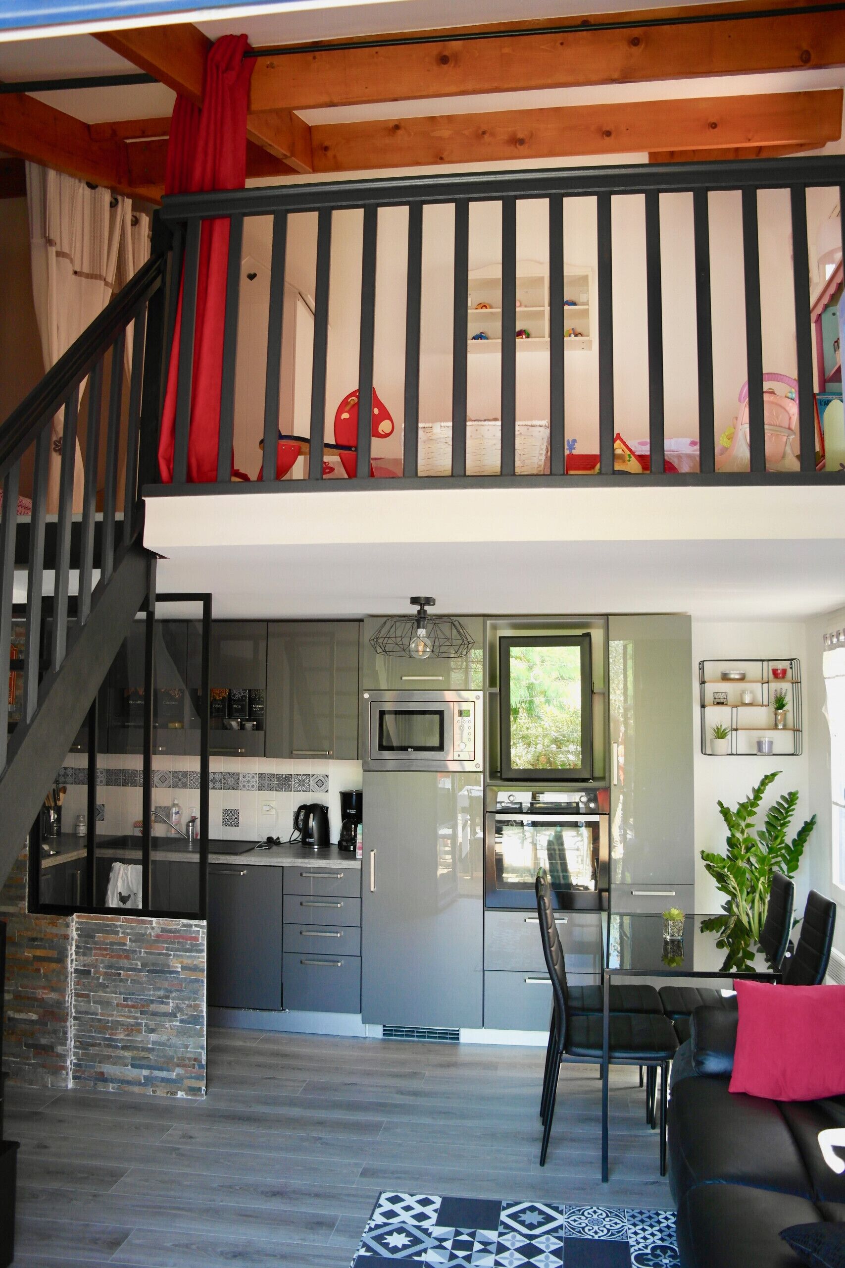A modern kitchen with a dining area, a staircase, and a loft bedroom with a red curtain.