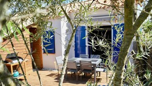A wooden deck with a table and chairs, a barbecue grill, and a blue door. - House for 4, close to the beach, shared pool (Saint-Hilaire-de-Riez)
