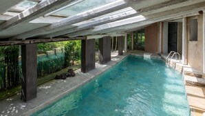An indoor swimming pool with clear water, supported by columns, and surrounded by a natural outdoor area. - Stunning private villa with WIFI, private pool, TV, terrace, pets allowed and panoramic view (Trezzo Tinella)