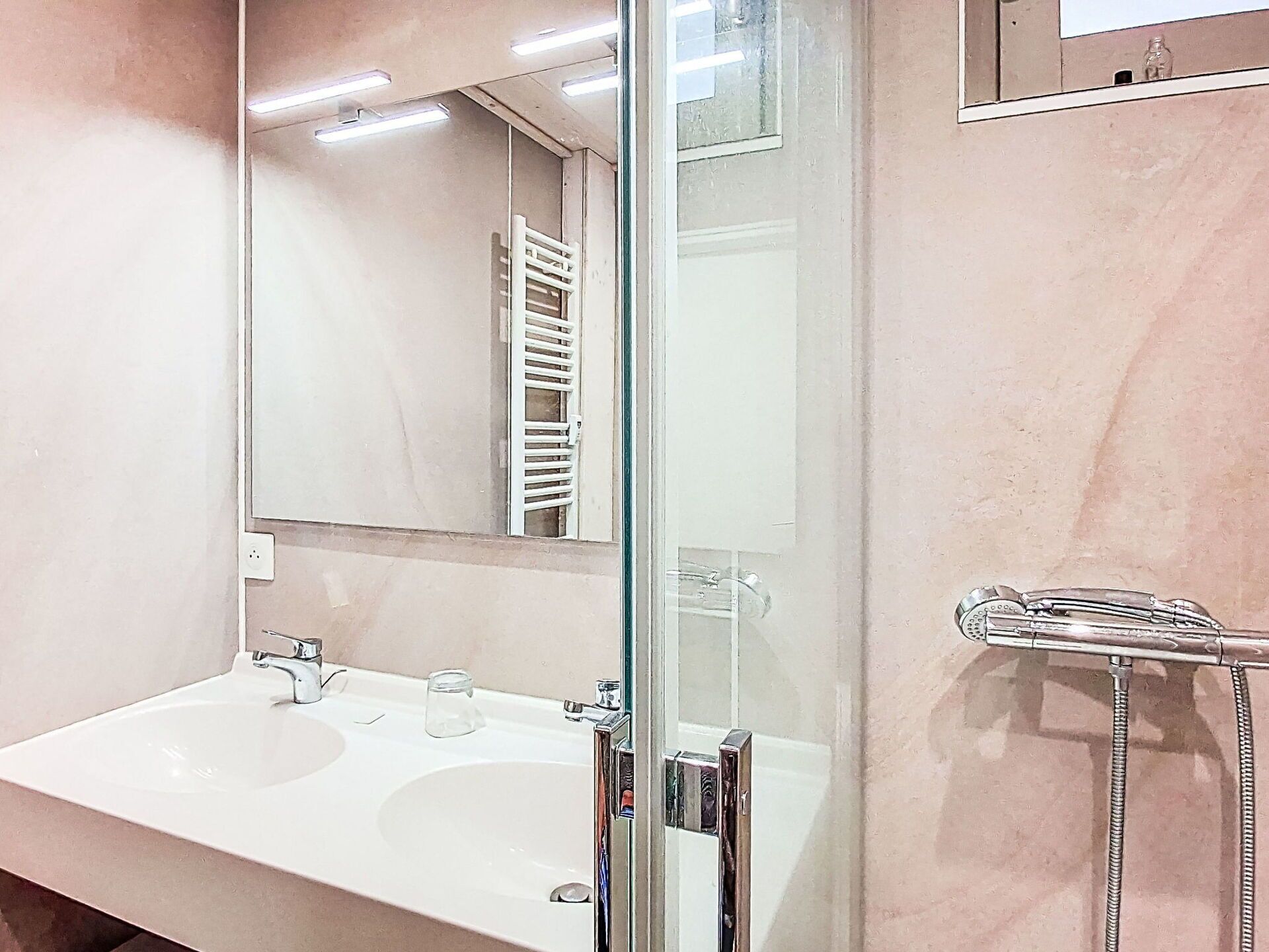 Une salle de bain avec un lavabo blanc, un miroir et une cabine de douche en verre.