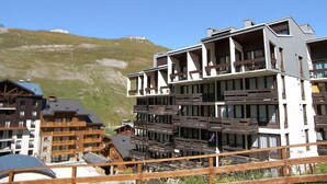 Ein modernes Hotel mit mehreren Balkonen und großen Fenstern, vor einer Bergkulisse gelegen.