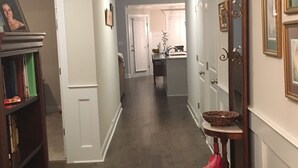 A hallway with wooden flooring, white walls, and a door leading to a kitchen area. - Beautiful House for the Masters (Grovetown)