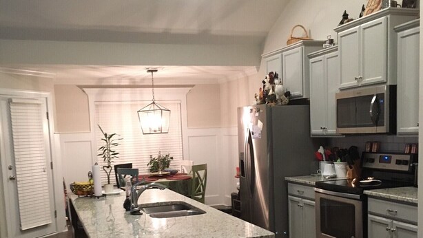 A modern kitchen with a central island, stainless steel appliances, and a dining area with a chandelier. - Beautiful House for the Masters (Grovetown)
