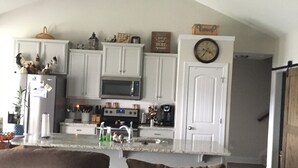 A modern kitchen with white cabinets, a microwave, and a clock on the wall. - Beautiful House for the Masters (Grovetown)