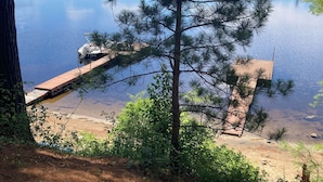 Une vue paisible sur un lac, avec une jetée s’avançant dans l’eau, entourée d’arbres et sous un ciel dégagé.