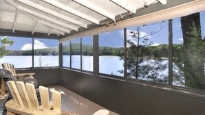 Un espace extérieur aménagé, abrité et doté de grandes fenêtres donnant sur un lac.