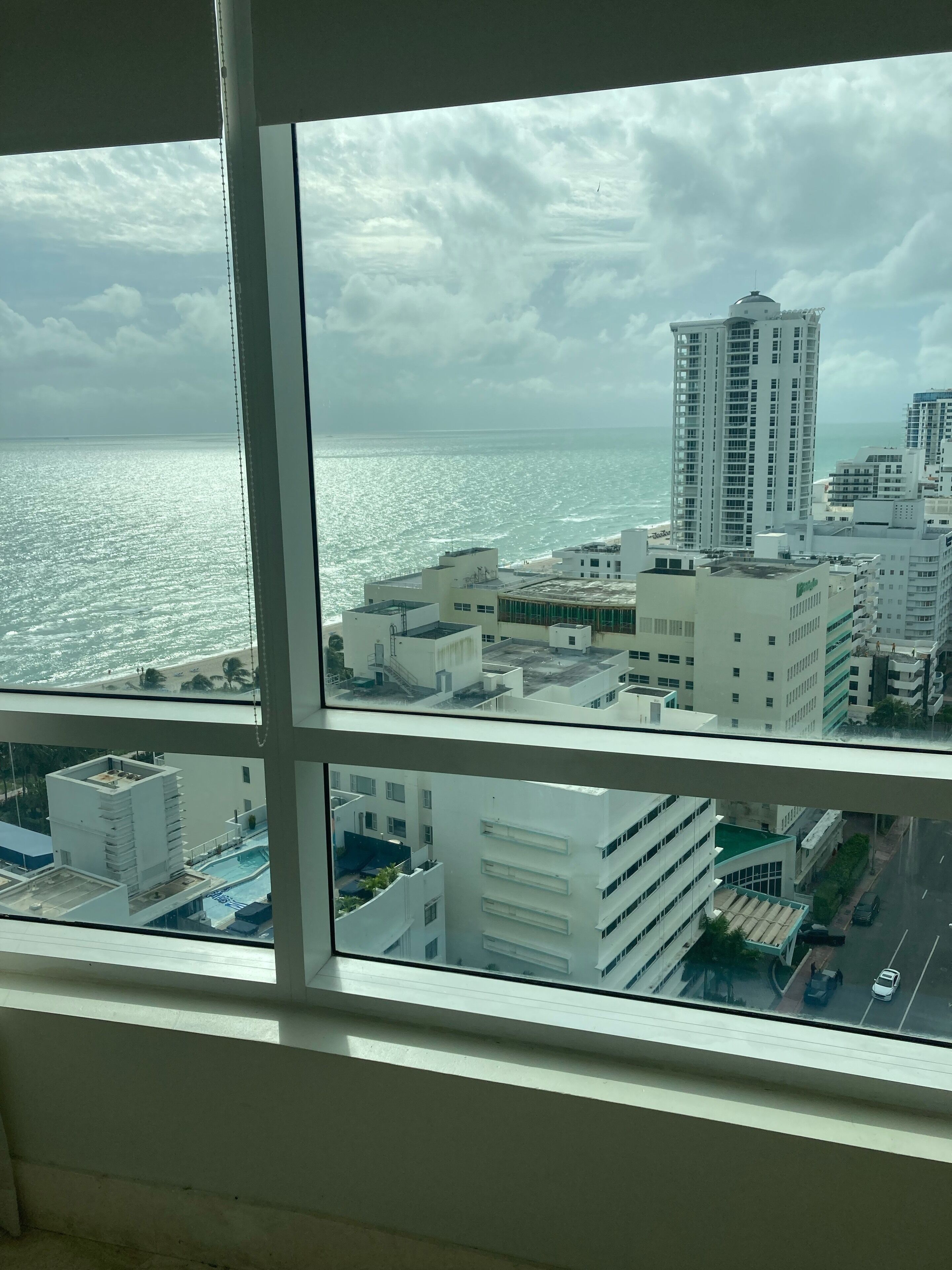A view through a window of a coastal cityscape with modern buildings, a clear sky, and a calm sea.
