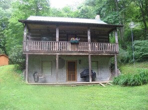 A rustic wooden cabin with a balcony, a front door, and a small porch area.
