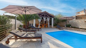 A swimming pool with lounge chairs and umbrellas, a covered seating area, and a stone wall. - Villa Parlera (Ližnjan)