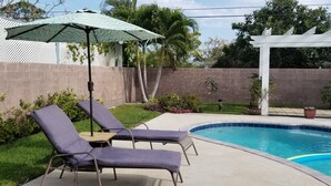 Un jardin avec une piscine, deux chaises longues, une table et un parasol.