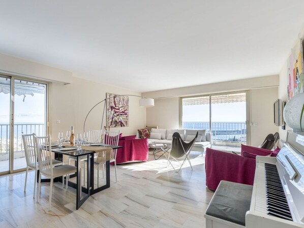 A spacious living area with a dining table, chairs, a piano, and a sofa.