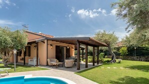 Una casa con piscina, mobiliario exterior y un patio cubierto.